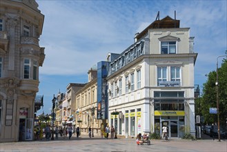 Sunny city scene with people walking on a street between traditional buildings, pedestrian zone