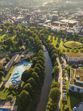 Urban overview with outdoor pool and riverbank, surrounded by trees and park-like green areas in