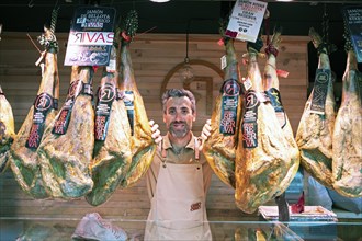 Castilian man, 40 years old, between Iberico hams for sale at the Mercado Central, Salamanca,