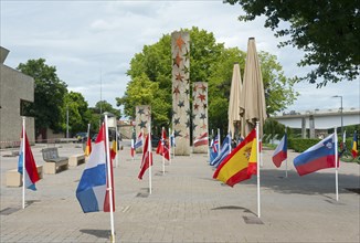 Flags of different countries in front of several pillars in an outdoor area, nation pillars in