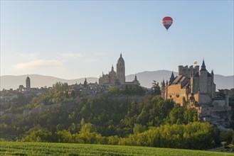 Beautiful view of a castle at sunrise with a hot air balloon in the sky and green fields in the