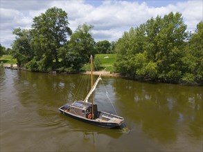 A lonely boat floats on a calm river, surrounded by green landscape and trees under a clear sky,