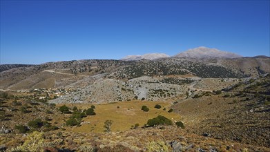 Vast landscape with mountains and sparse vegetation under a bright blue sky, Lefka Ori, White