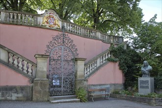 Entrance to the garden through metal gate with coat of arms and monument with bust of Annette von