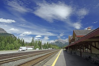 Railway tracks next to a station with mountain landscape and cloudy sky in the background, Banff,