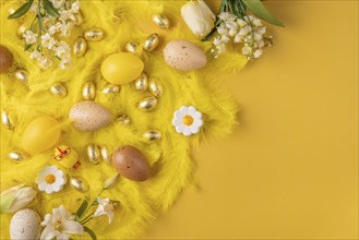 Festive Easter decorations with yellow feathers, yellow Easter eggs and spring flowers on a yellow