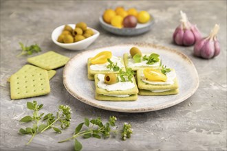 Green cracker sandwiches with cream cheese and cherry tomatoes on gray concrete background. side