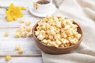 Popcorn with caramel in wooden bowl and a cup of coffee on a white wooden background and linen