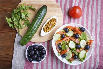 Vegetarian salad of tomatoes, cucumbers, parsley, olives and mustard on linen tablecloth, top view,