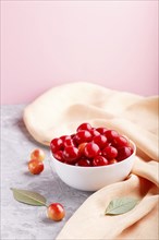 Fresh red sweet cherry in white bowl on gray and pink background with orange textile. side view,