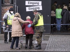 A Bundeswehr soldier helps an elderly woman arriving at the vaccination centre in the Arena in