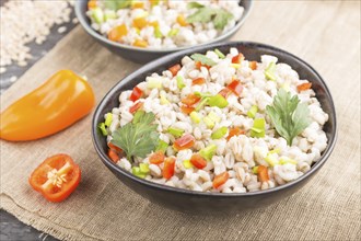 Pearl barley porridge with vegetables in blue ceramic bowls on a black concrete background and