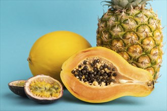 Ripe cut papaya, pineapple, melon, passion fruit, on blue pastel background. Side view, close up.