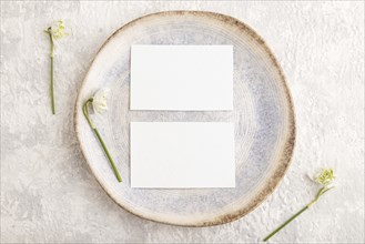 White paper invitation card, mockup with galanthus snowdrop flowers on ceramic plate and gray