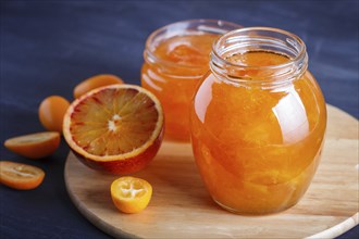 Orange and kumquat jam in a glass jar with fresh fruits on a wooden kitchen board. Homemade, close