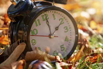 Symbolic image time change, autumn: An alarm clock among autumn leaves