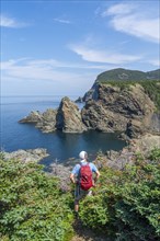 Hiker stands at a viewpoint above the rocky coast in Bottle Cove Provincial Park, Bay of Islands,