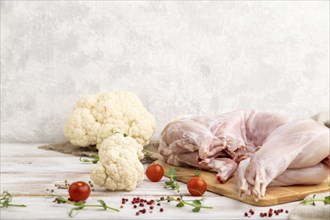 Whole raw rabbit with cauliflower, tomatoes and spices on a white wooden background and linen