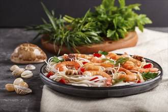 Rice noodles with shrimps or prawns and small octopuses on gray ceramic plate on a black concrete