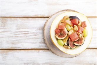 Vegetarian fruit salad of watermelon, grapes, figs, pear, orange, cashew on white wooden background