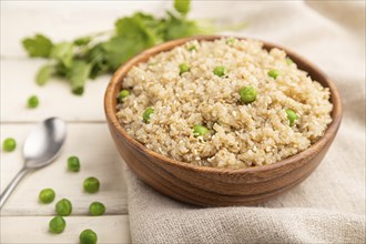 Quinoa porridge with green pea in wooden bowl on a white wooden background and linen textile. Side