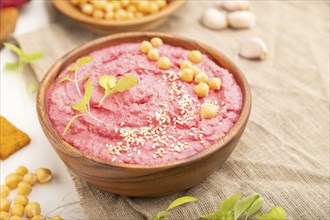 Hummus with beet and microgreen basil sprouts in wooden bowl on a white wooden background and linen