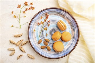 Orange macarons or macaroons cakes with cup of coffee on a white concrete background and linen