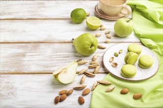 Green macarons or macaroons cakes with cup of coffee on a white wooden background and green linen