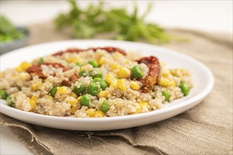 Quinoa porridge with green pea, corn and dried tomatoes on ceramic plate on a white wooden