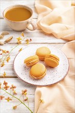 Orange macarons or macaroons cakes with cup of apricot juice on a white wooden background and