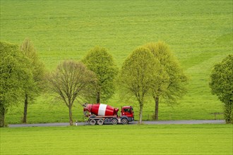 Concrete mixer truck on a country road, green fields, meadows, trees line the 2-lane road, spring,