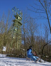 Winter in the Ruhr area, toboggan run on a forest path at Lake Baldeney, headframe of the former