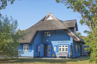 A picturesque, blue-painted thatched roof house with bench in front of the entrance, open door,