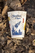 Discarded McDonald's take-away drink carton cup on floor on top of leaf litter, 'Christmas is here'