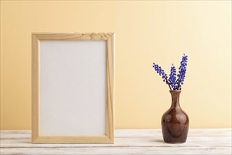 Wooden frame with blue muscari hyacinth flowers in ceramic vase on orange pastel background. side