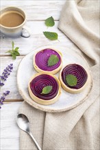 Sweet tartlets with jelly and milk cream with cup of coffee on a white wooden background and linen