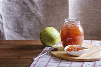 Pear jam in a glass jar on a linen tablecloth on a wooden table. Homemade, copy space