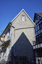 Narrow, slate-panelled house with a pointed roof and shade against a cloudless blue sky on the