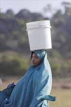 Woman with a bucket of water on her head in Maraban Dare community, Plateau state, 07/02/2024