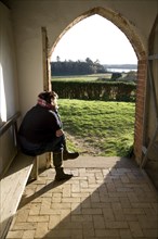 Model released woman sitting in church porch looking at the view over the River Deben, Ramsholt,