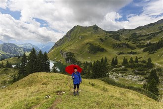 Woman 60-65 hiking with umbrella, behind her Seealpsee and Seeköpfel, 1919m, Allgäu Alps, Allgäu,