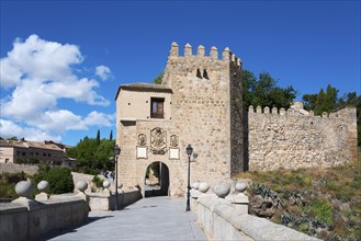 Old stone castle with neighbouring bridge under a blue sky, surrounded by green plants, Puente de