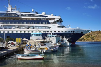 A large cruise ship moored in the harbour of a Greek island, surrounded by smaller fishing boats on