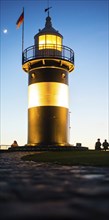 Black and white lighthouse, called 'Kleiner Preuße', stands illuminated in the evening against a