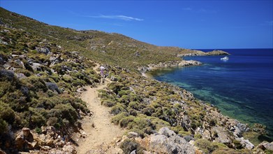 A hiking trail along a rocky coastline with views of the clear sea and blue sky, path to Psili