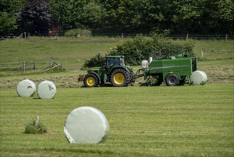 Hay harvest, farmer with agricultural machine, picks up mown hay, which is immediately pressed into