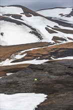 Green tent in a dramatic volcanic landscape with mountains and snow, at Höskuldsskáli hut in