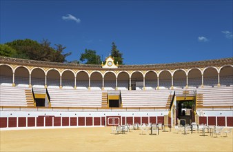 Historic bullring with classic architecture and blue sky, sandy floor and chairs in the centre,