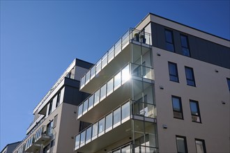 Modern residential building with glass balconies under a blue sky and reflecting sunlight, Molde,