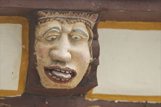 Wood carving with envious head symbolising gluttony, excess, intemperance, face, tongue, nose,